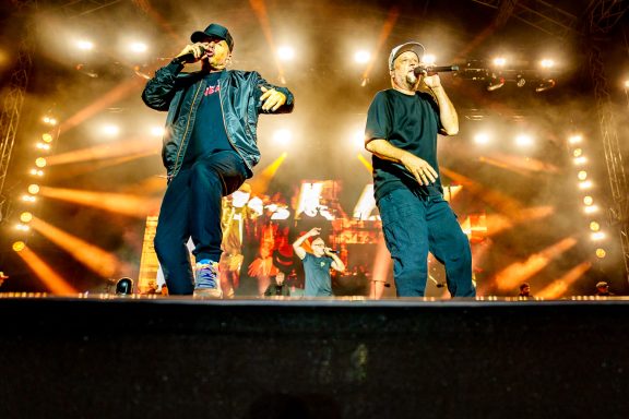 Zwei Männer performen live auf der Bühne mit buntem Licht im Hintergrund.